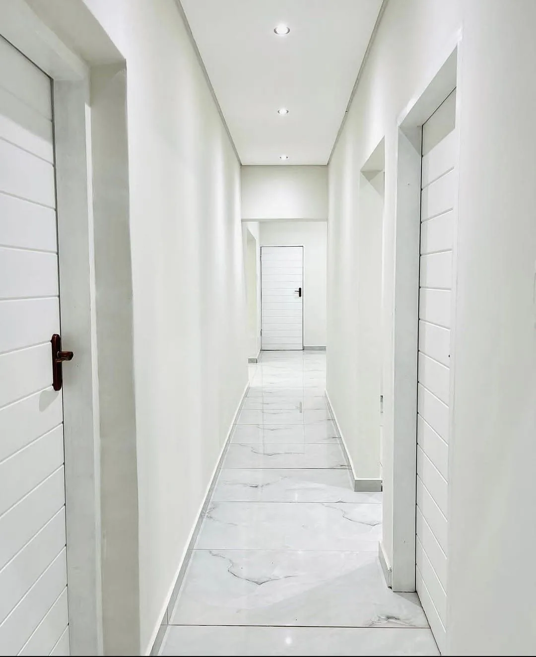 Bright hallway renovation with white doors and tile flooring